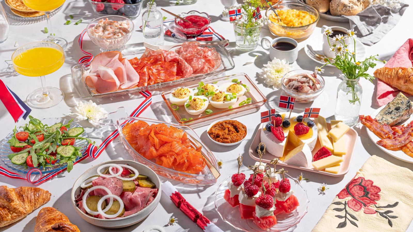 Et bord dekket med ulike frokostretter og kaker, inkludert røkelaks, eggerøre, salat og små kaker, sannsynligvis til 17. mai-feiring.