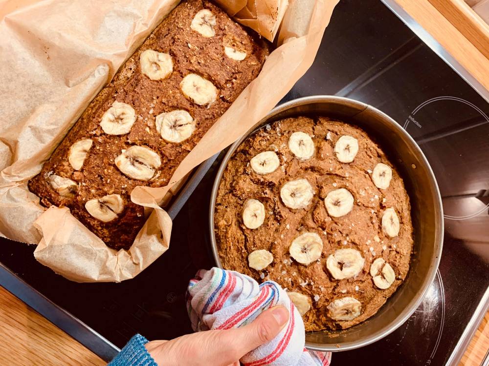 Banankake i en ildfast form og en stekepanne med bananskiver på toppen, klar til å serveres.