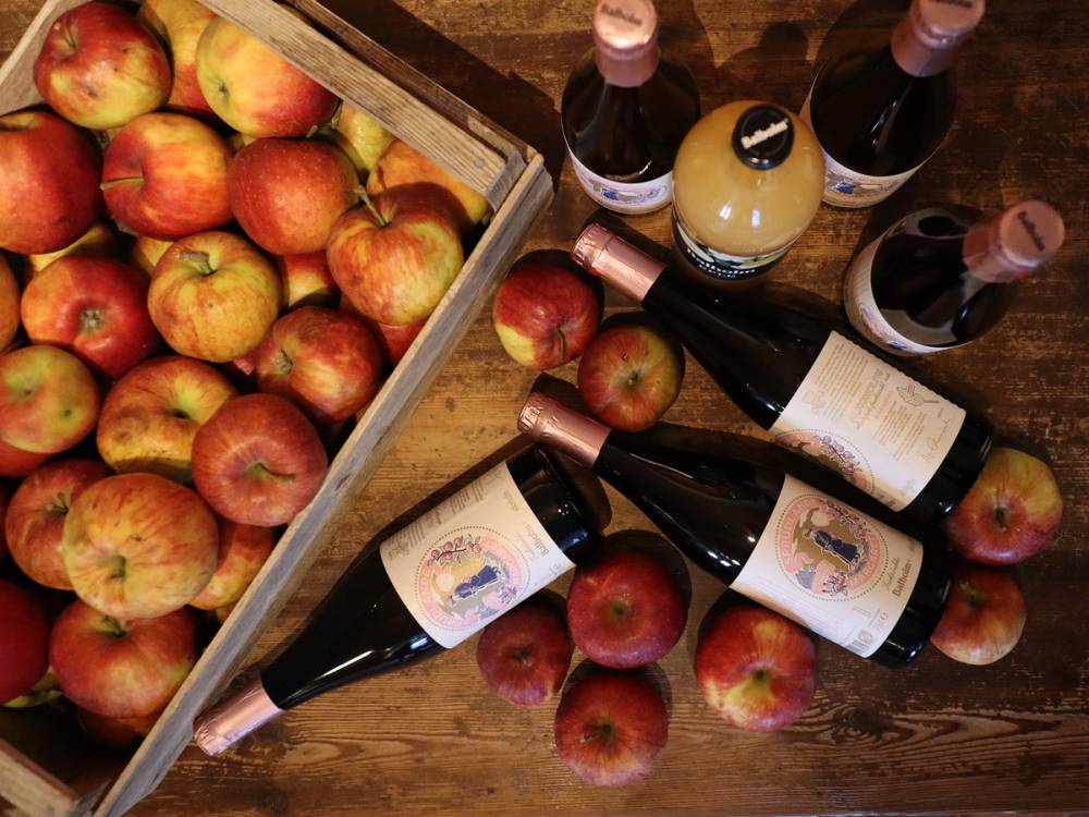 Epler og flasker med drikkevarer ligger på et bord, med noen epler spredt rundt.