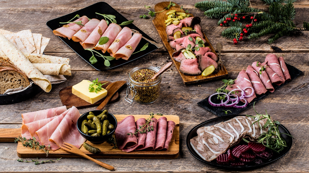 Ulike typer kjøttpålegg og påskefat med brød og tilbehør på et bord, dekorert med julegrener.