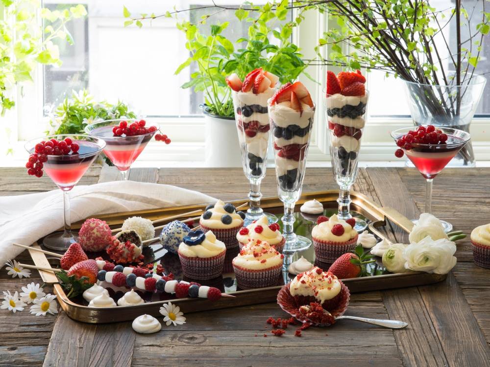 Et utvalg av små kaker og desserter på et bord med grønne planter i bakgrunnen.