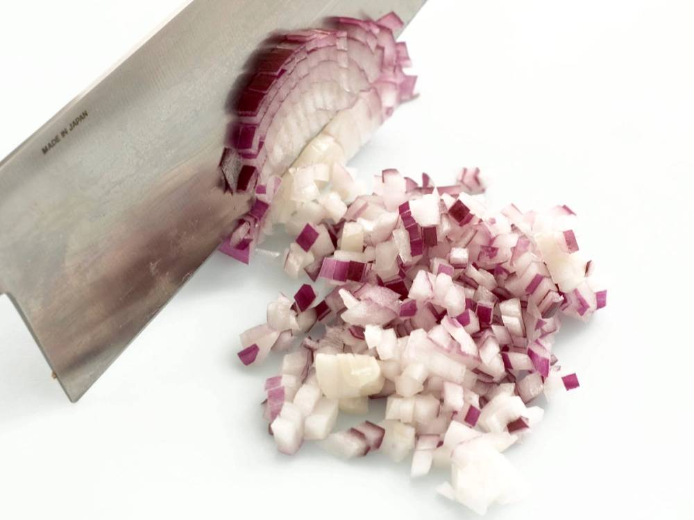 Finhakket rød løk på skjærebrett med en stor kniv ved siden av.