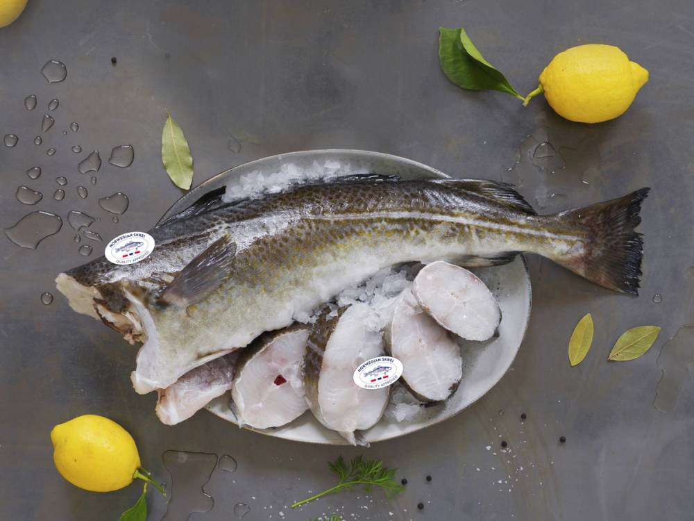 Skrei-fisk på en tallerken med sitroner og urter rundt, klar for tilberedning.