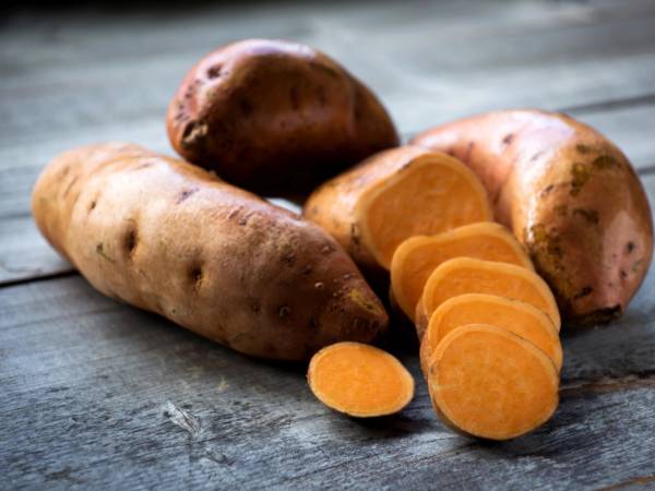 Noen søtpoteter, hvorav noen er skrellet og skiver, ligger på en treflate.