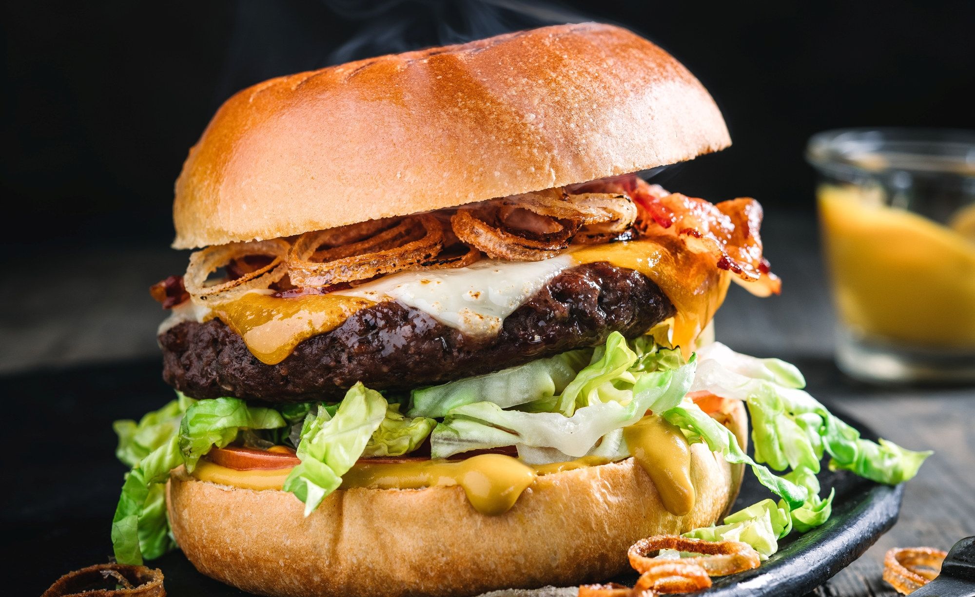 En saftig hamburger med kjøttkake, ost, bacon, salat og dressing i et brød, med en liten skål med saus ved siden av.