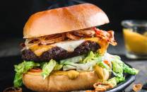 En saftig hamburger med kjøttkake, ost, bacon, salat og dressing i et brød, med en liten skål med saus ved siden av.