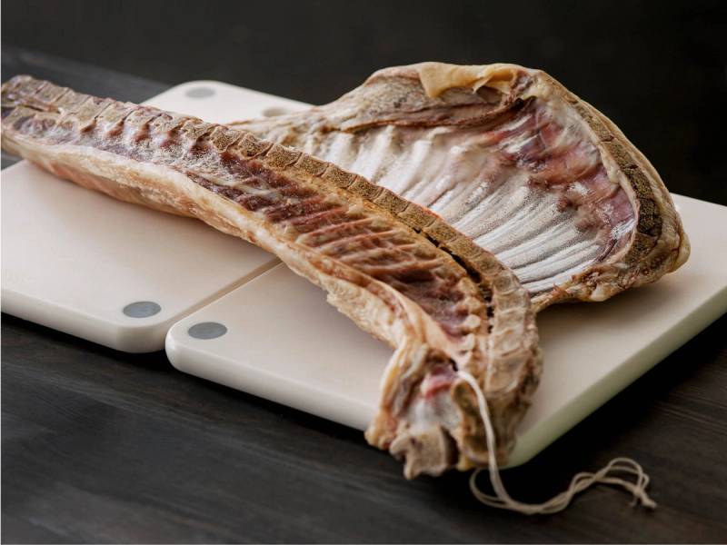 Pinnekjøttside med bein ligger på en skjærebrett, klar til tilberedning.