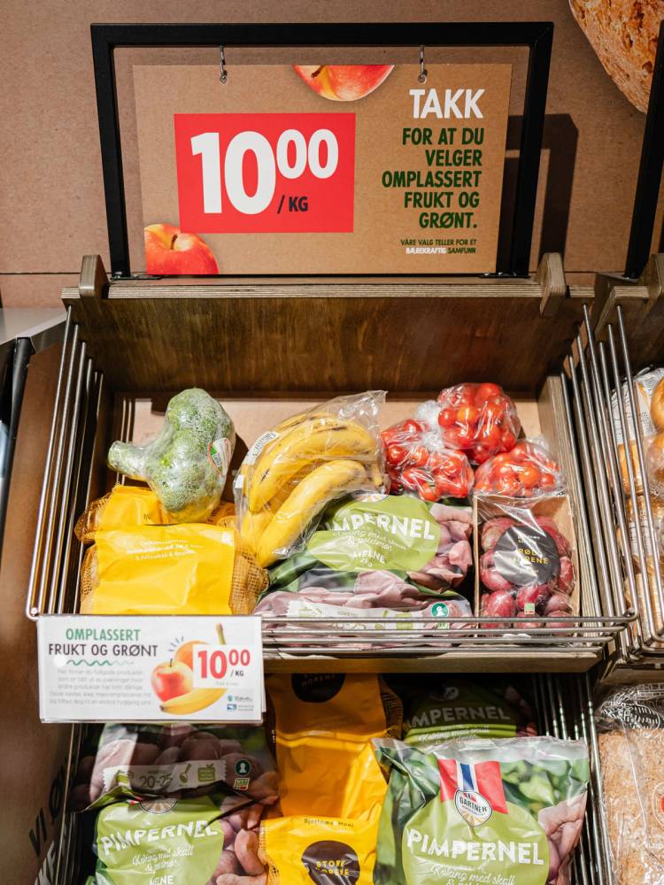 En frukt- og grønnsaksdisk med bananer, epler og andre frukter, med en prisskilt som viser 10,00 kr per kilo.