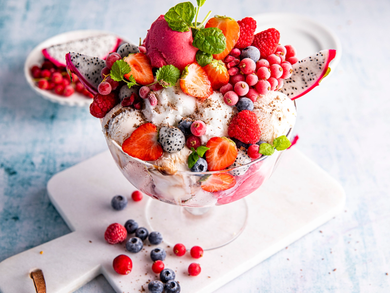 En vegansk festdessert med iskrem og ferske bær i en glasskål, pyntet med mynteblader.