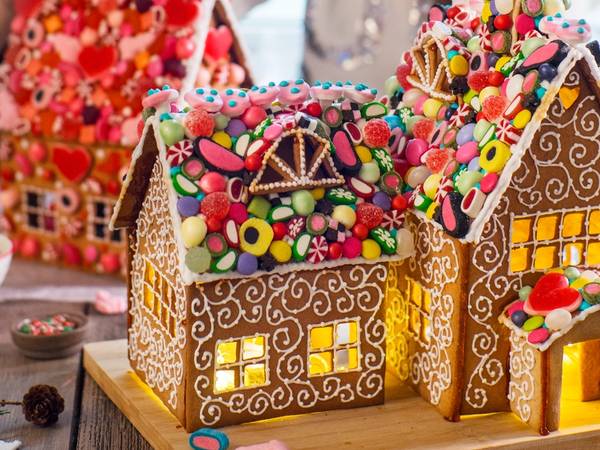 Et pyntet pepperkakehus med fargerike godteri og lysende vinduer på et bord med småkaker og pynt rundt.