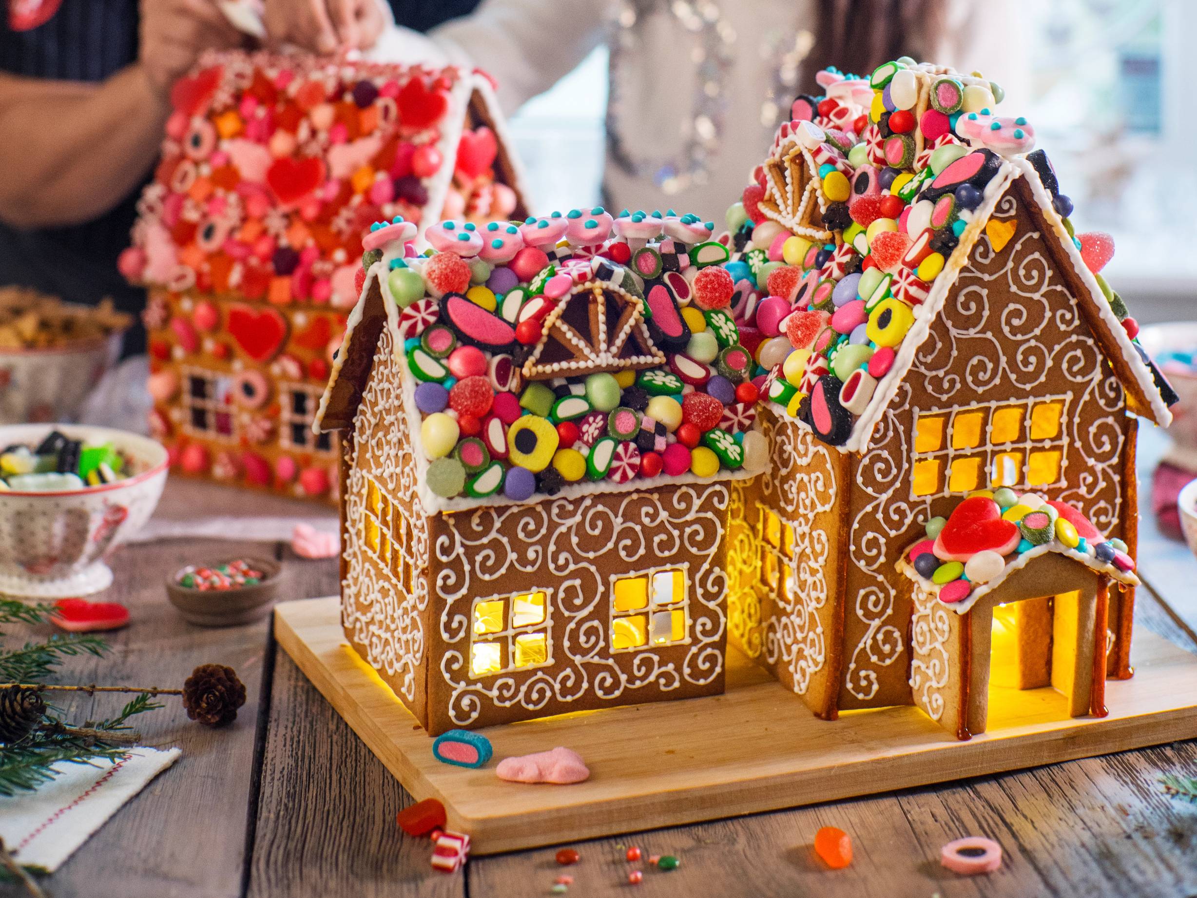 Et pyntet pepperkakehus med fargerike godteri og lysende vinduer på et bord med småkaker og pynt rundt.