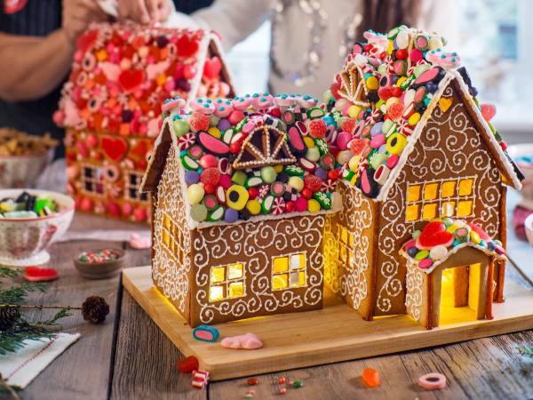 Et pyntet pepperkakehus med fargerike godteri og lysende vinduer på et bord med småkaker og pynt rundt.
