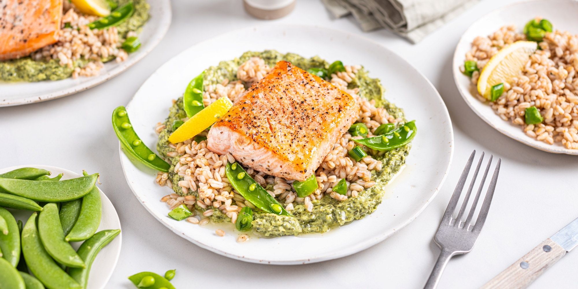 Laks med grønnkålkrem servert på en hvit tallerken, omgitt av grønnsaker og tilbehør på bordet.