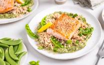 Laks med grønnkålkrem servert på en hvit tallerken, omgitt av grønnsaker og tilbehør på bordet.