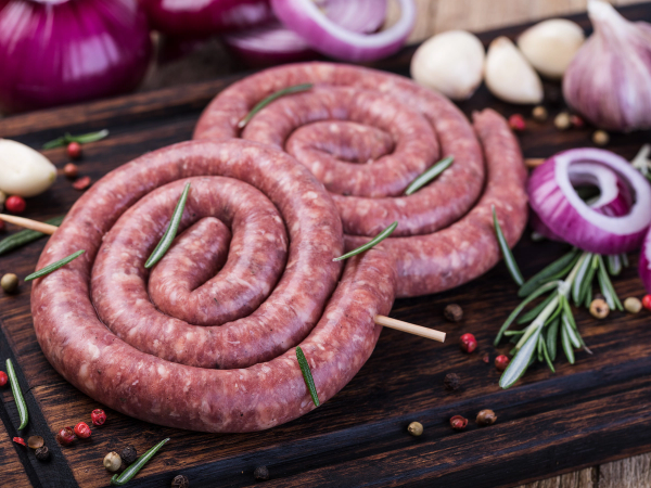 Rundstykker av pølse ligger på en skjærefjøl med urter og krydder rundt.