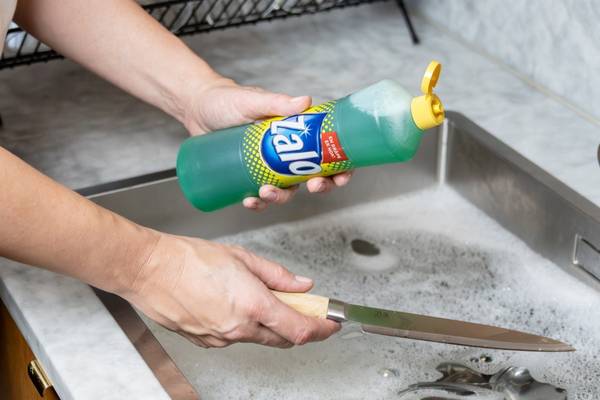 Person vasker opp i en kjøkkenkum med zalo-såpe, og bruker en svamp eller klut til å vaske oppvasken.