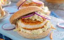 Fiskeburger med coleslaw og skiver av rødløk i et brød, servert på en lys skjæreflate.