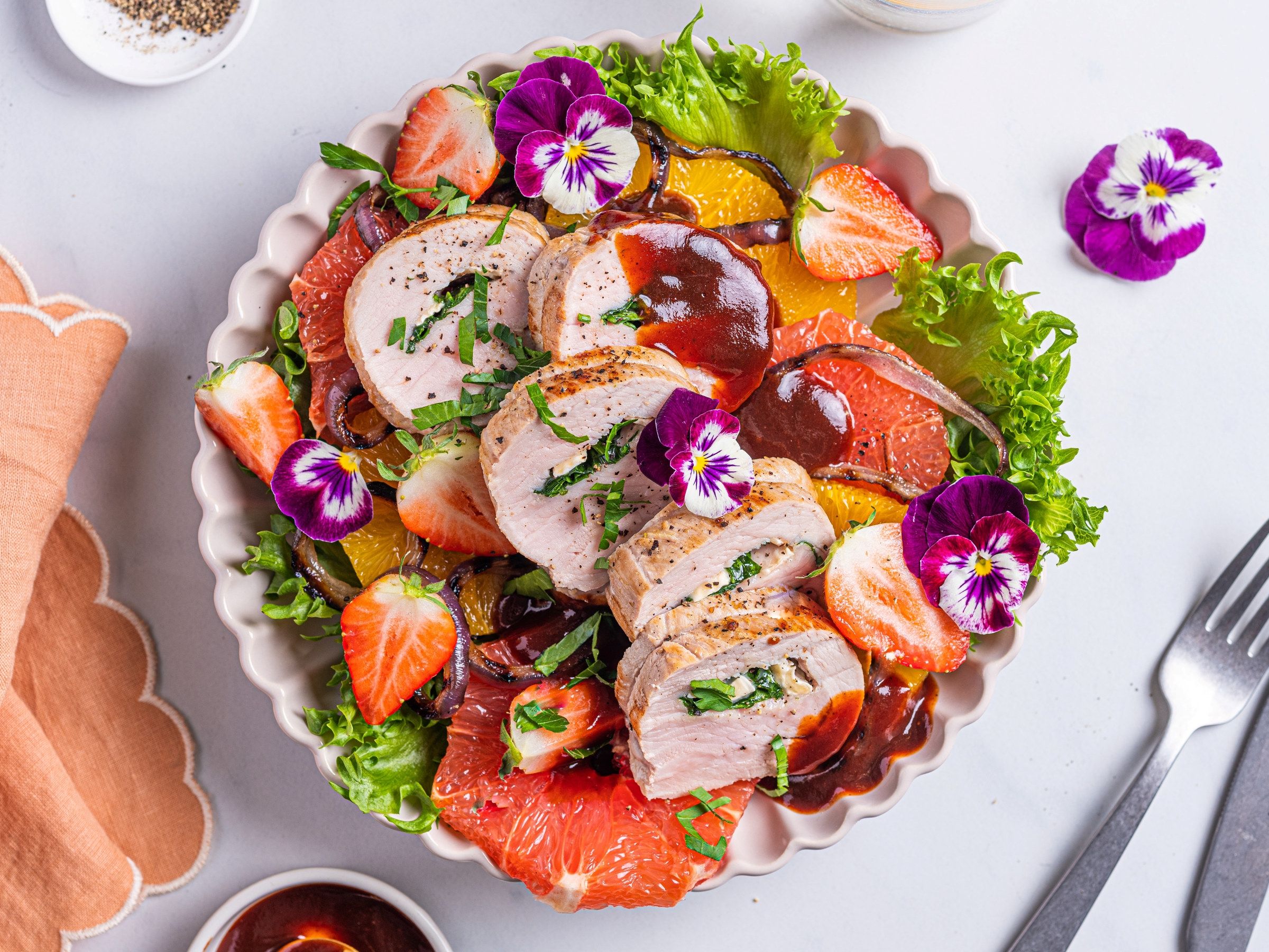 Svinefilet fylt med ost og spinat, servert med en salat av jordbær, appelsinbiter og grønn salat, pyntet med spiselige blomster.