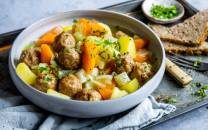 En bolle med kjøttboller, gulrøtter, poteter og grønnsaker, servert med brød ved siden av.