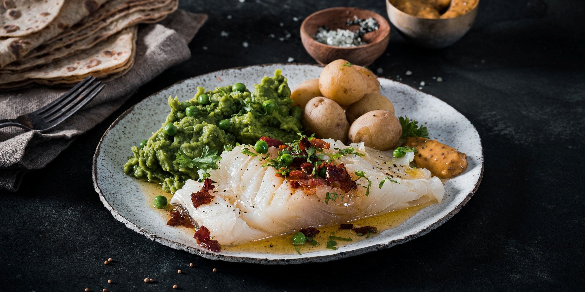 Lutefisk servert med grønnsaker og små poteter på en hvit tallerken.