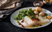 Lutefisk servert med grønnsaker og små poteter på en hvit tallerken.