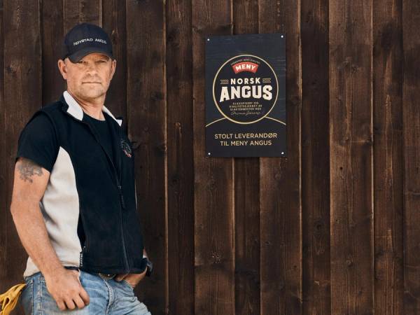Svein Eberhard Østmoe foran låveveggen med norsk Angus-skiltet.