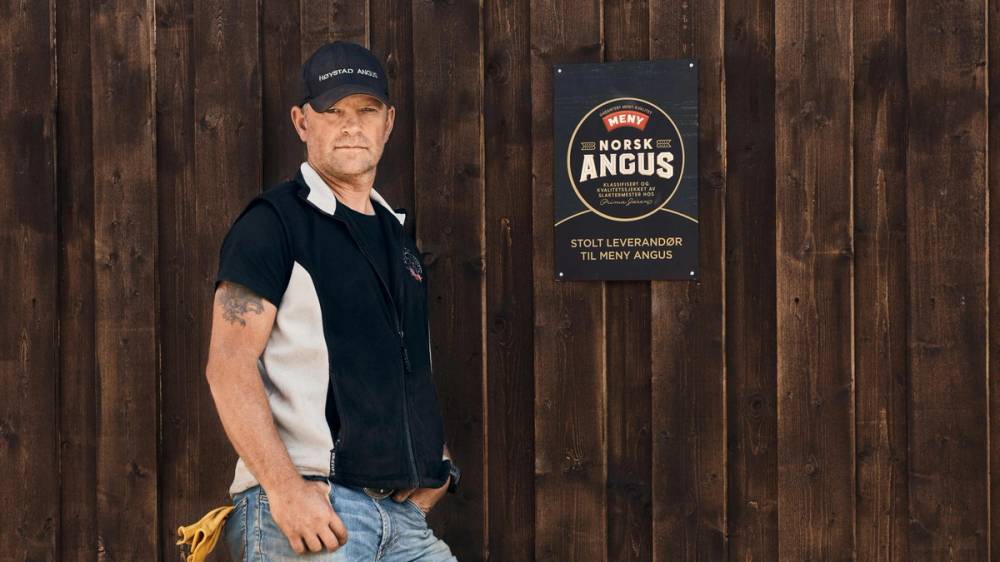 Svein Eberhard Østmoe foran låveveggen med norsk Angus-skiltet.