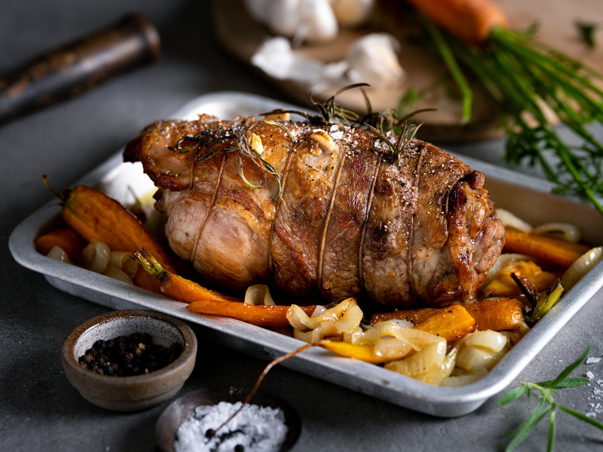 Klassisk lammestek med grønnsaker på en hvit serveringsfat, omgitt av urter og krydder, klar til å serveres.