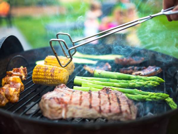 Grill med kylling, maiskolber, asparges og biff som blir grillet utendørs.