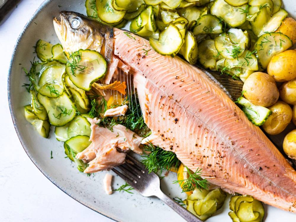 En hel, kokt telemarksrøye med poteter og agurksalat på en tallerken.