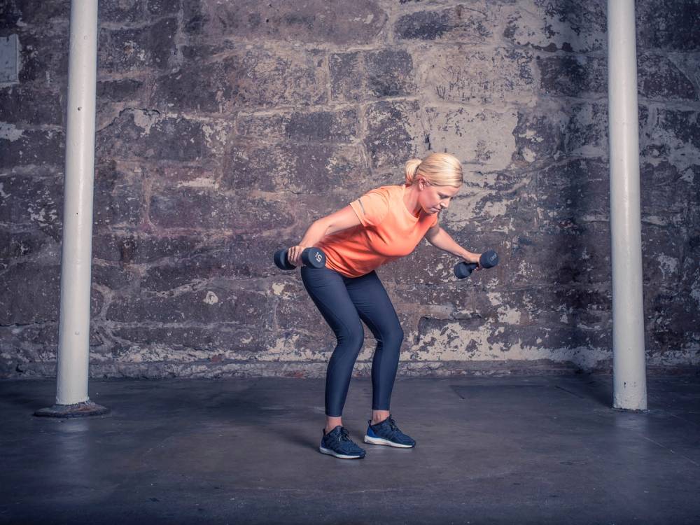 En person bøyer seg fremover med armene ut til sidene foran en murvegg, som om de er i ferd med å falle eller gjøre en øvelse.