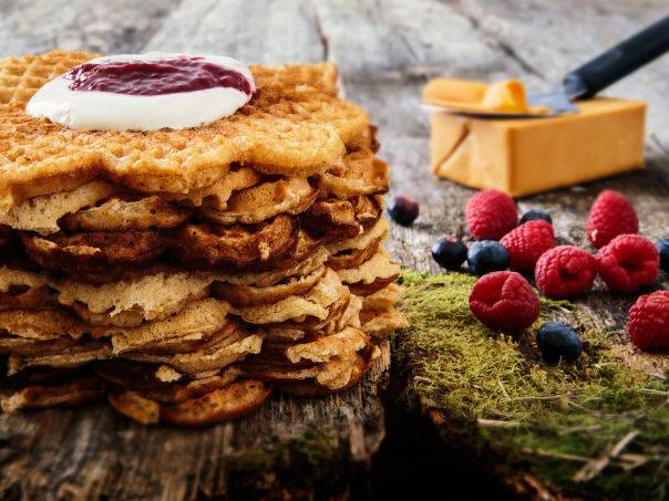 Grove vafler med syltetøy og friske bær på et fat, med en tresleiv i bakgrunnen.