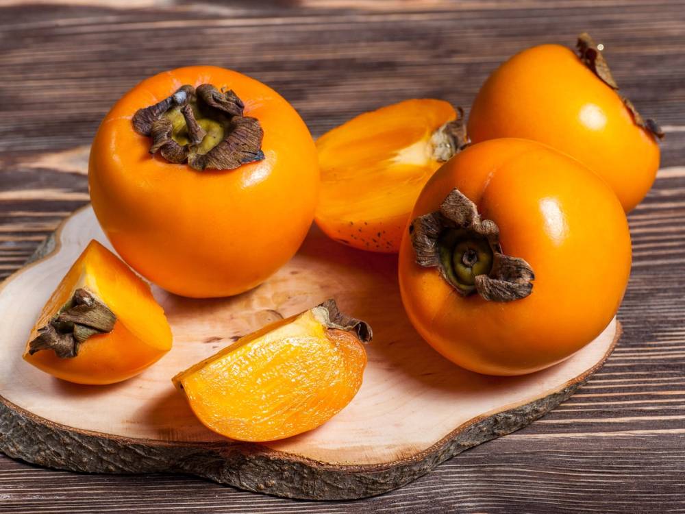 Fire persimmonfrukter, hvorav noen er skåret opp, ligger på et rundt trestykke på en treoverflate.