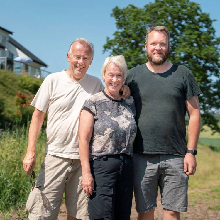 Tre personer står ute i solskinn med grønne trær og en bygning i bakgrunnen, alle med ansiktene dekket til.