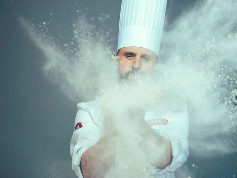 Roar med mel som kaster mel i luften under en matlagingsaktivitet, med melstøv som sprer seg rundt ham.