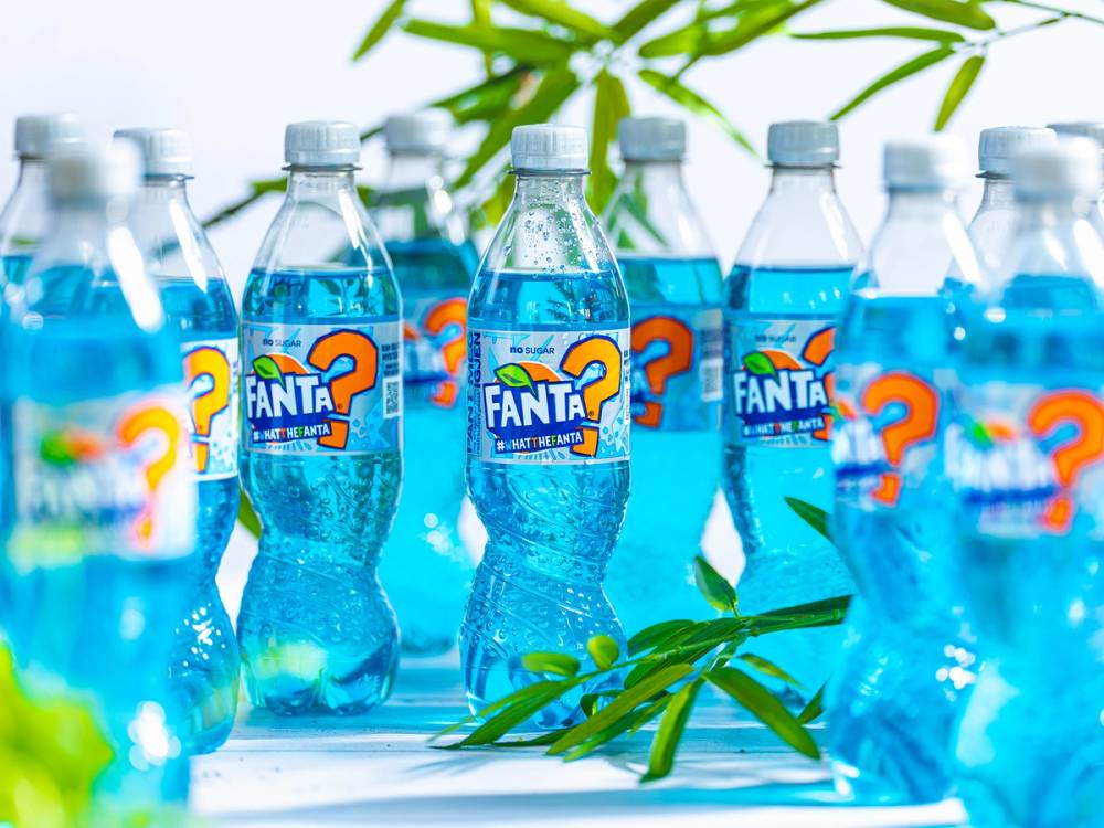 Flere Fanta-flasker med blå væske står på et bord med grønne blader rundt omkring.