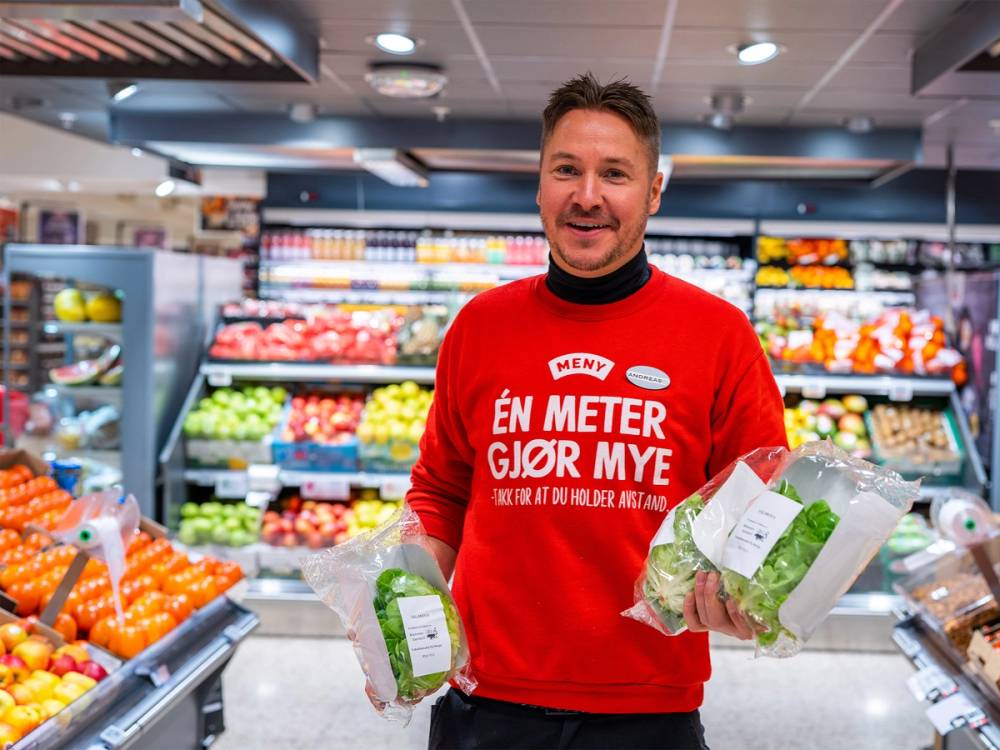 En mann i en rød genser som står i en dagligvarebutikk med grønnsaker i hendene.