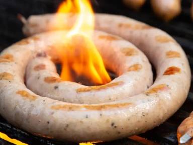 Rå pølse som ligger på grillen med flammer rundt, klar til å bli stekt.