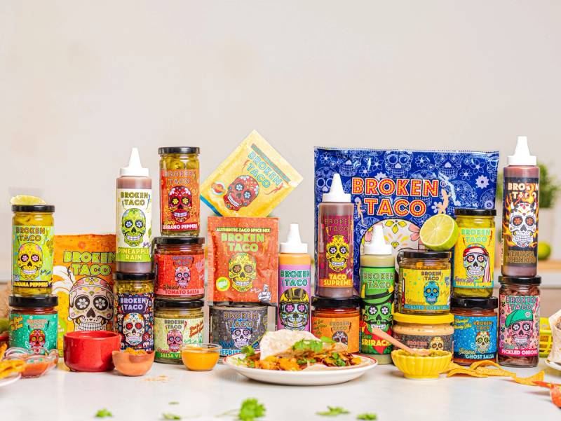 Et utvalg av forskjellige fargerike matprodukter og tilbehør, inkludert en taco, på et bord.