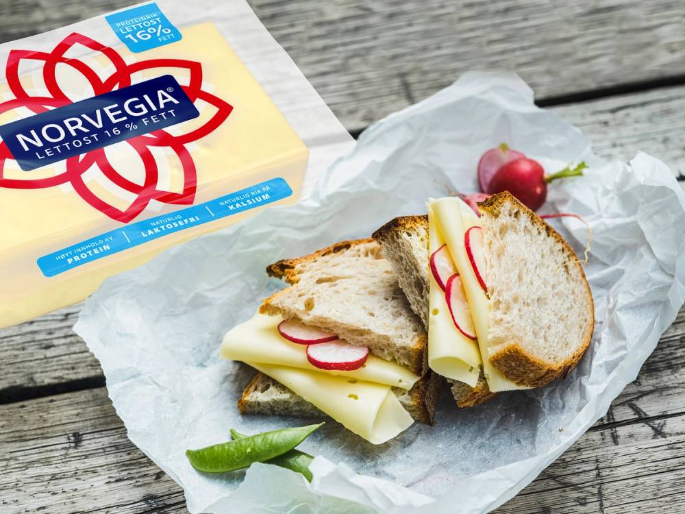 Lettostykke med radiser og salat på et stykke brød, med Norvegia-ostepakke i bakgrunnen.