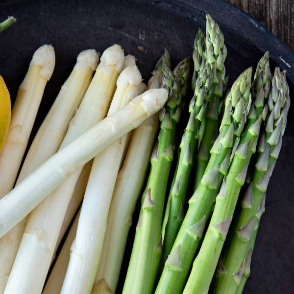 Hvite og grønne asparges ligger på en svart tallerken.