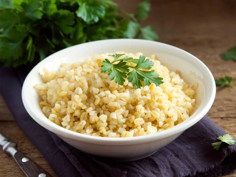 Bulgur i en hvit bolle med fersk persille på toppen, plassert på en mørk duk på et bord.