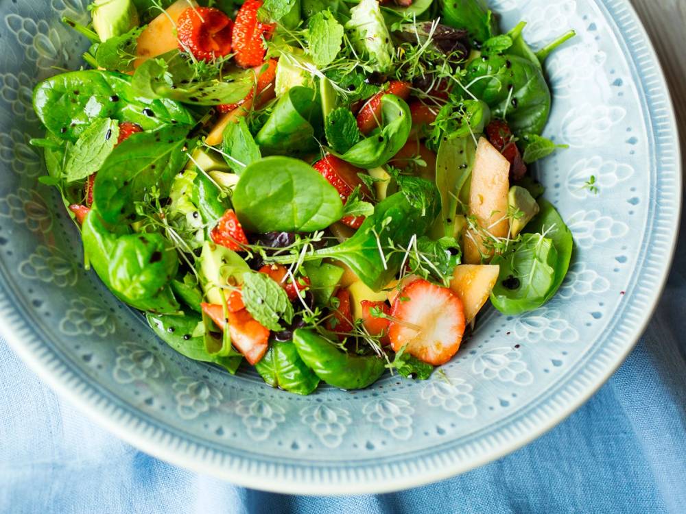 En frisk salat med jordbær, melonbiter og avokadoskiver i en blå serveringsskål.