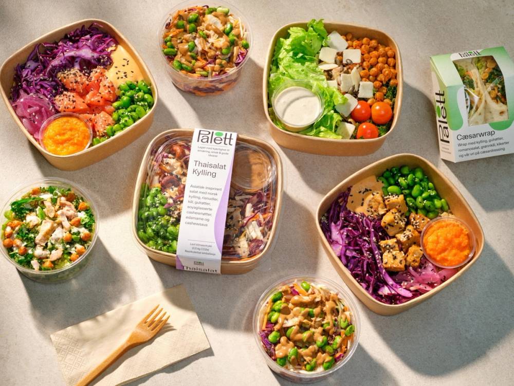 En samling av ulike matretter i plastbokser og skåler, inkludert salat, ris, grønnsaker og en eggerøre, på et bord.