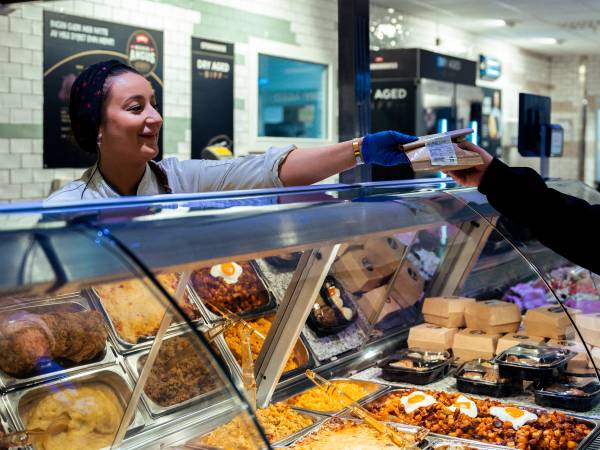 Kjøtt- og påleggsavdeling i en dagligvarebutikk med en ansatt som hjelper en kunde, uten å vise ansiktet til personen.