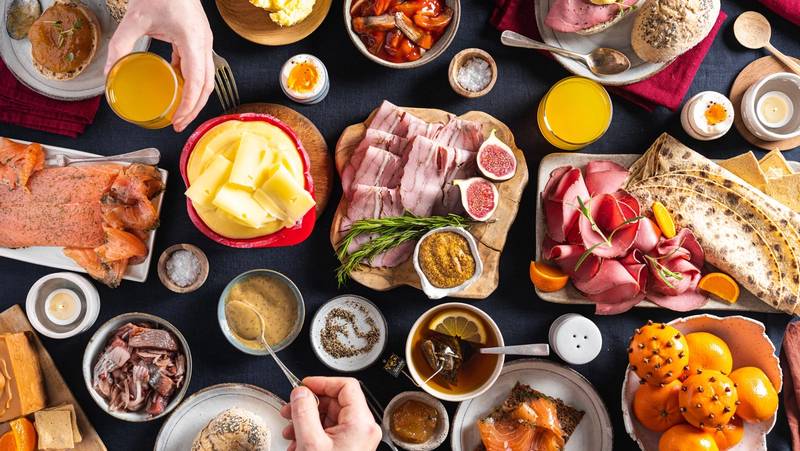 Et julefrokostbord med ulike retter, pølser, pålegg, egg, og frukt, sett fra oven.