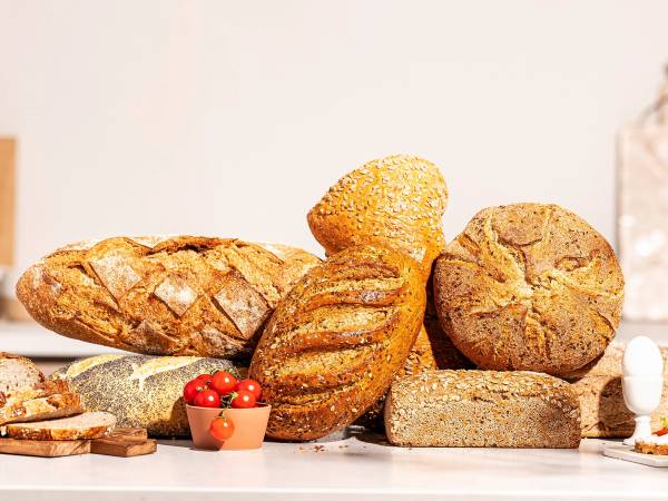 Ulike typer brød og bakverk på et bord, med en liten skål med tomater foran.