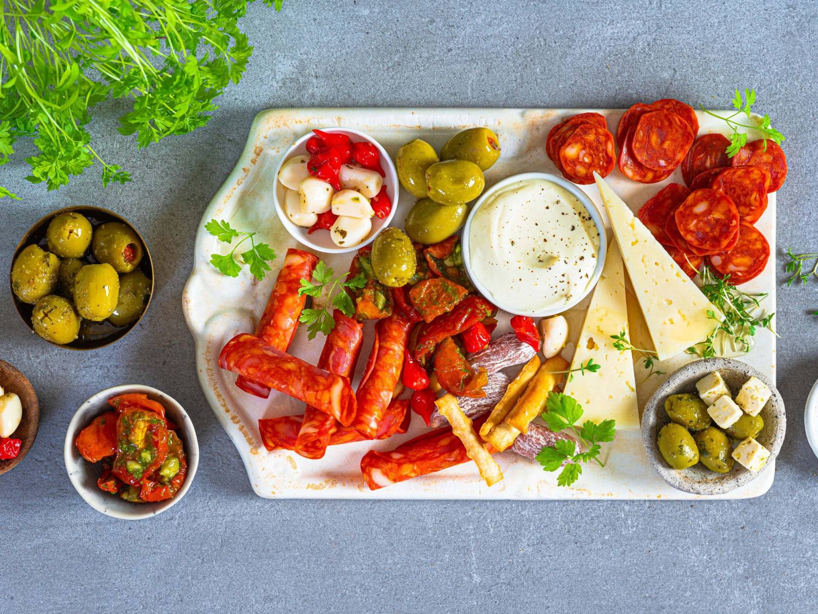 Et fat med ulike typer tapas, inkludert oliven, cherrytomater, ost, og grønnsaker, på en lys bakgrunn.