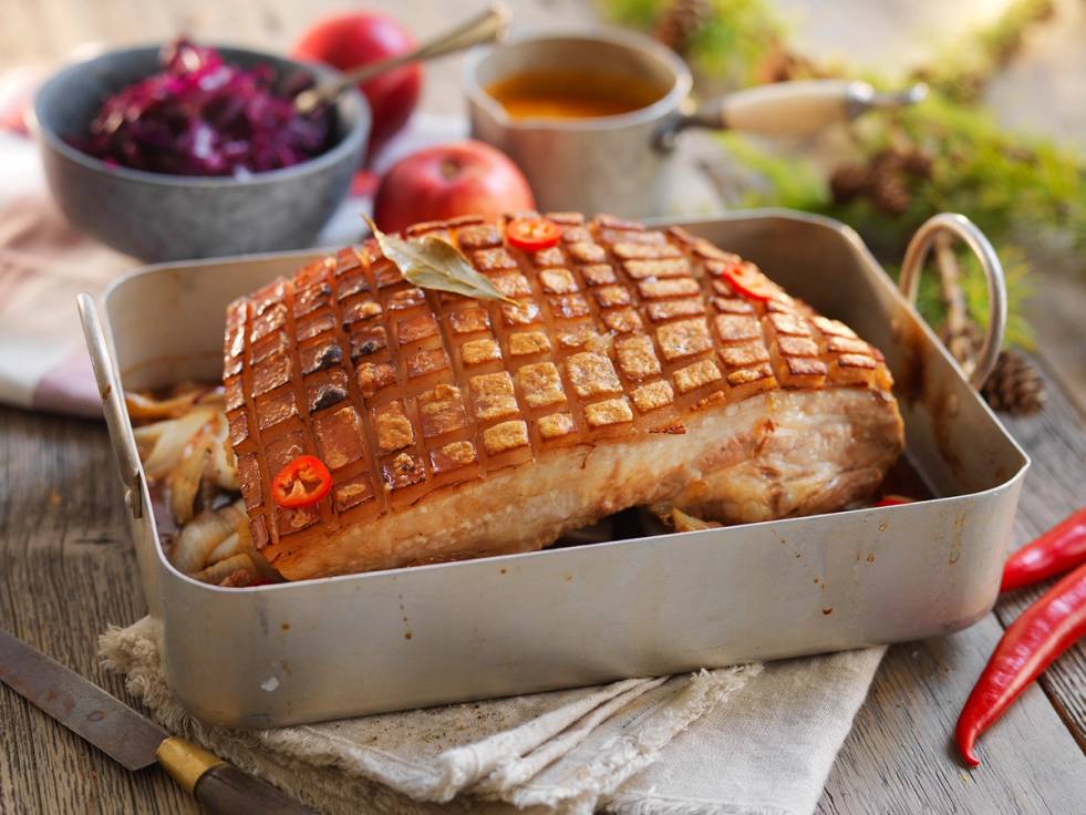 Ribbe med chili i en ildfast form, omgitt av grønnsaker og tilbehør, klar for servering.