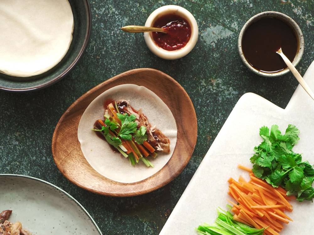 Kylling med grønnsaker og saus på en tallerken, omgitt av ulike sauser og grønnsaker på bordet.